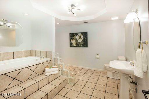 bathroom featuring tile patterned floors, a relaxing tiled tub, toilet, and a raised ceiling