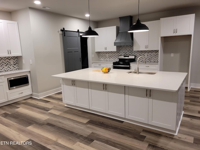 kitchen featuring sink, a barn door, an island with sink, custom range hood, and appliances with stainless steel finishes