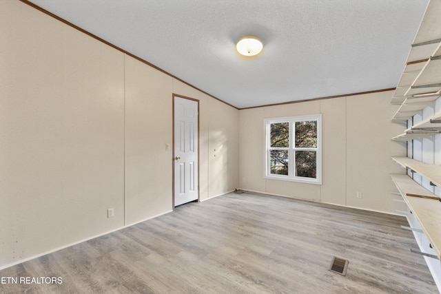 unfurnished room with vaulted ceiling, light wood-type flooring, a textured ceiling, and ornamental molding