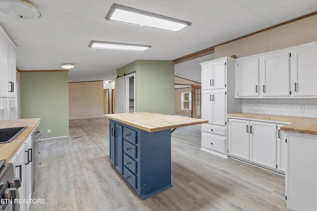 kitchen with butcher block counters, white cabinetry, a barn door, light hardwood / wood-style flooring, and backsplash