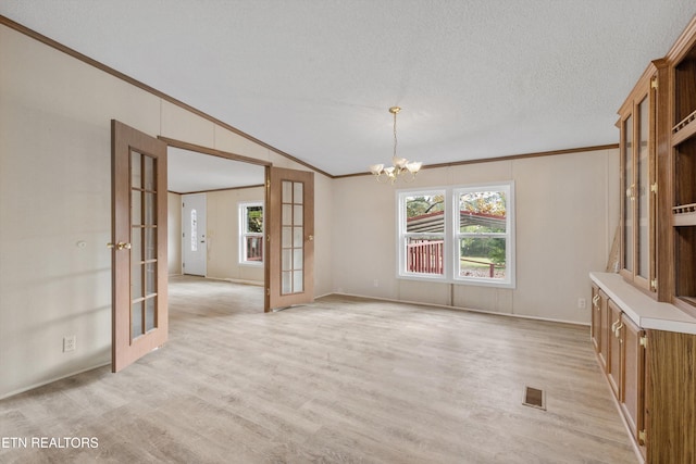 unfurnished room featuring french doors, ornamental molding, a textured ceiling, vaulted ceiling, and a chandelier