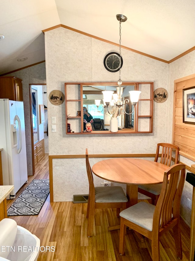 dining area with crown molding, a notable chandelier, vaulted ceiling, and light wood-type flooring