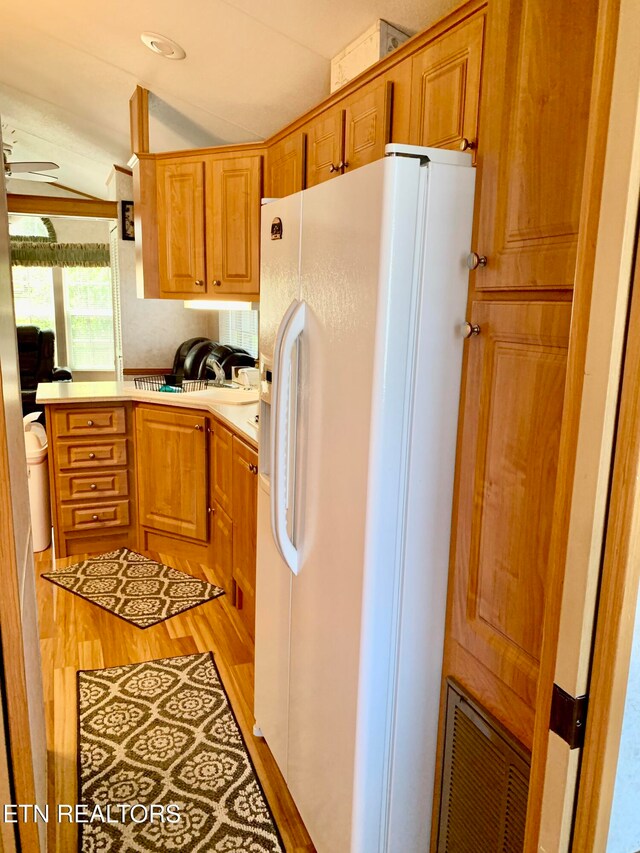 kitchen with ceiling fan, white fridge with ice dispenser, sink, light hardwood / wood-style floors, and vaulted ceiling