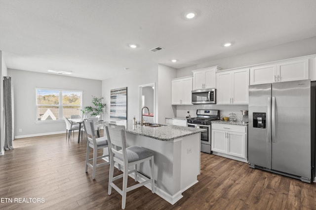 kitchen with appliances with stainless steel finishes, dark hardwood / wood-style flooring, white cabinetry, and an island with sink