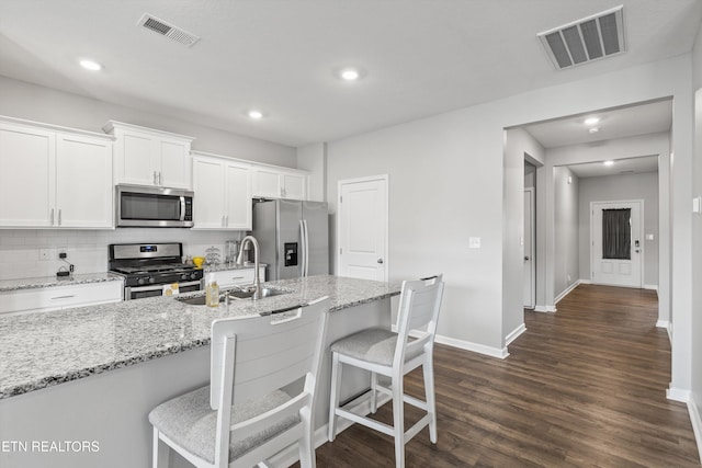 kitchen with light stone counters, dark hardwood / wood-style floors, a kitchen bar, white cabinets, and appliances with stainless steel finishes