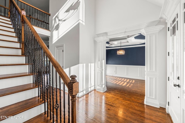 stairway with hardwood / wood-style floors, a towering ceiling, and decorative columns