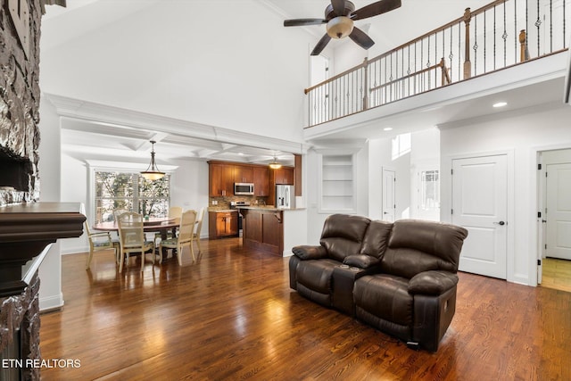 living room with dark hardwood / wood-style floors, ceiling fan, a towering ceiling, and beam ceiling