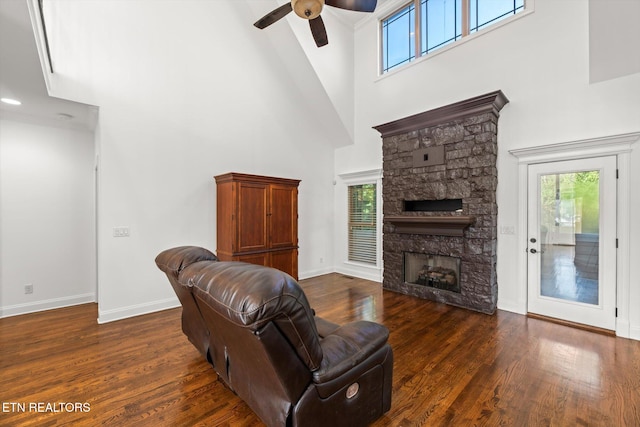 living room featuring ceiling fan, a stone fireplace, dark wood-type flooring, and a high ceiling