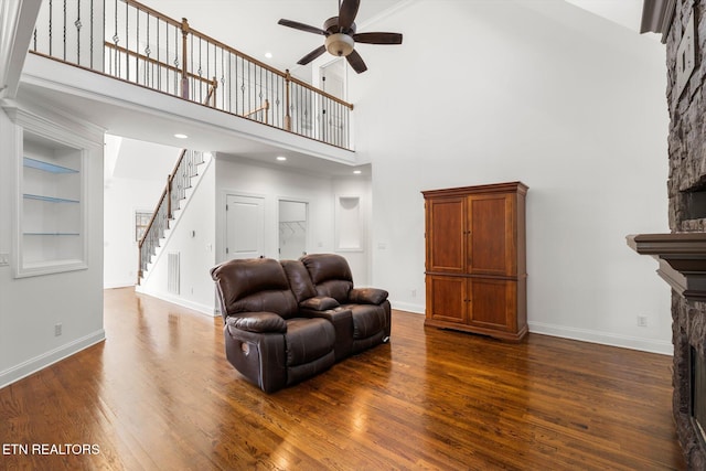 living room with a high ceiling, built in shelves, ceiling fan, a fireplace, and dark hardwood / wood-style flooring