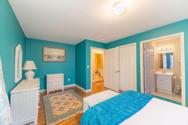 bedroom featuring ensuite bathroom, light wood-type flooring, and a closet