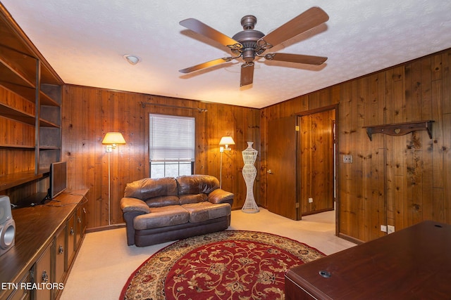 living room with wooden walls, ceiling fan, light colored carpet, and a textured ceiling