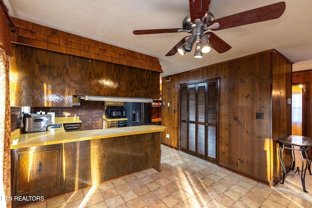 kitchen with black appliances, ceiling fan, wood walls, and kitchen peninsula