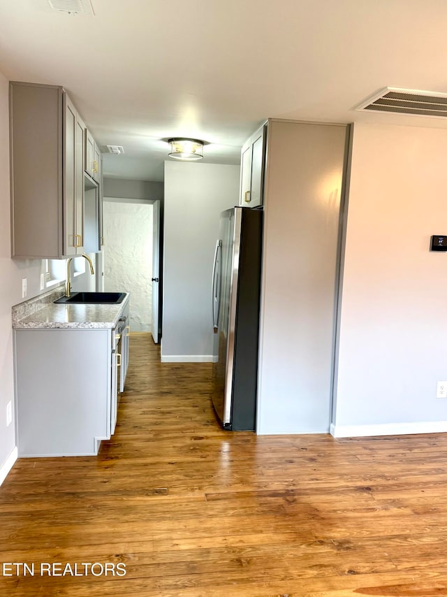 kitchen featuring stainless steel fridge, light hardwood / wood-style flooring, light stone countertops, and sink