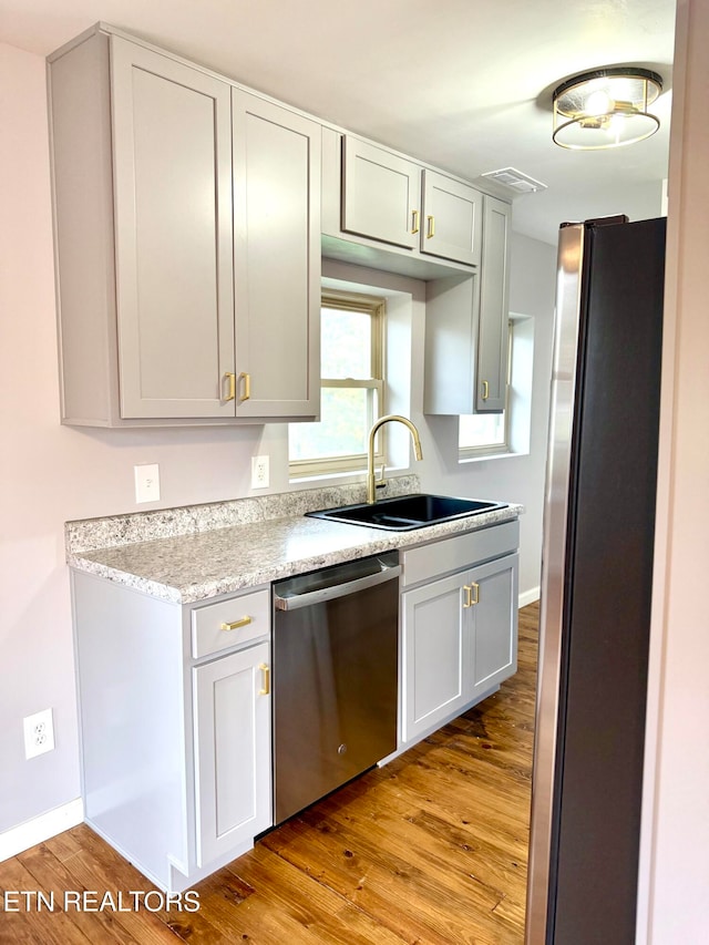 kitchen featuring appliances with stainless steel finishes, light wood-type flooring, light stone counters, and sink