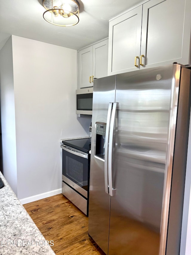 kitchen with stainless steel appliances, white cabinetry, and hardwood / wood-style flooring