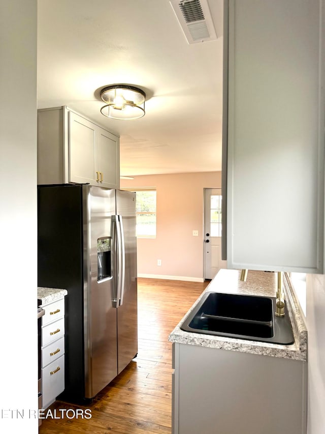 kitchen with sink, stainless steel refrigerator with ice dispenser, light stone countertops, light hardwood / wood-style floors, and white cabinetry