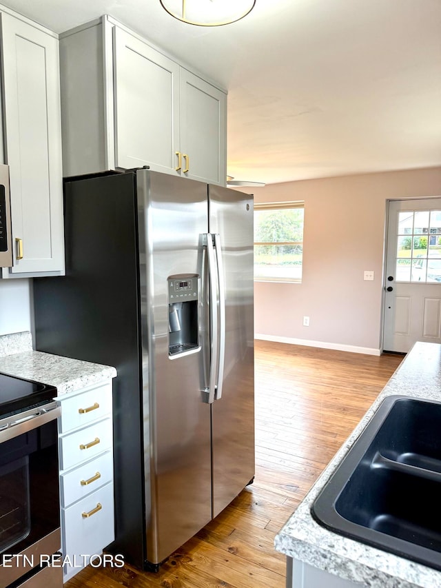 kitchen featuring white cabinets, appliances with stainless steel finishes, light hardwood / wood-style floors, and a healthy amount of sunlight