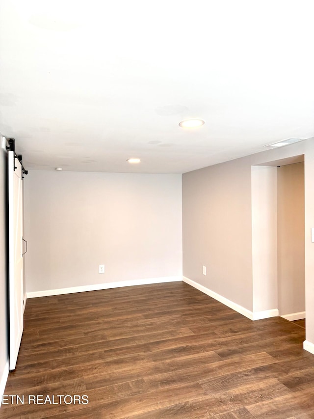 empty room with a barn door and dark hardwood / wood-style flooring