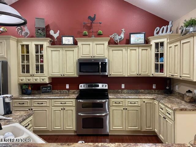 kitchen featuring light stone countertops, dark hardwood / wood-style floors, cream cabinets, lofted ceiling, and appliances with stainless steel finishes