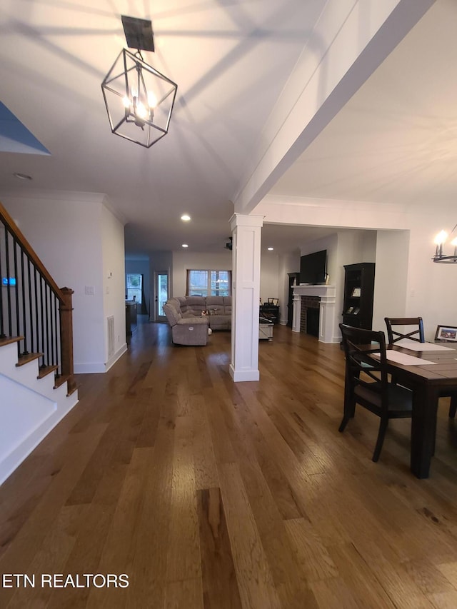 dining space with ornate columns, stairway, an inviting chandelier, and dark wood-style flooring