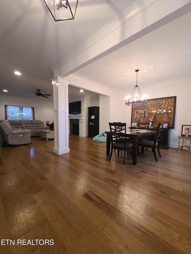 dining space featuring hardwood / wood-style floors, ceiling fan with notable chandelier, ornate columns, and a fireplace