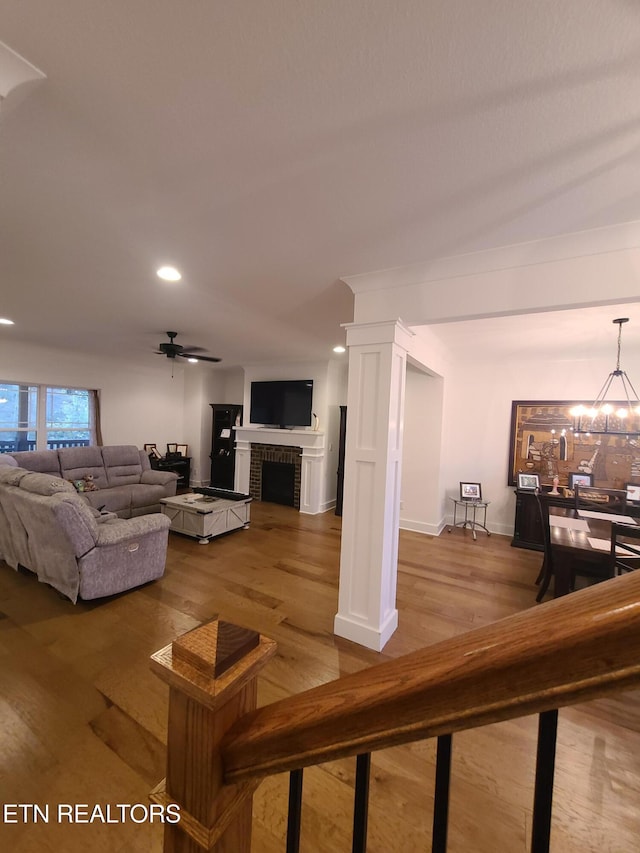 living room featuring recessed lighting, ceiling fan with notable chandelier, a fireplace, wood finished floors, and ornate columns