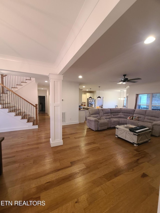 living area with stairway, visible vents, a ceiling fan, and wood finished floors