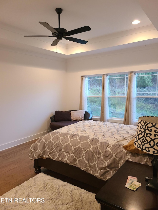 unfurnished bedroom with baseboards, a tray ceiling, recessed lighting, wood finished floors, and a ceiling fan