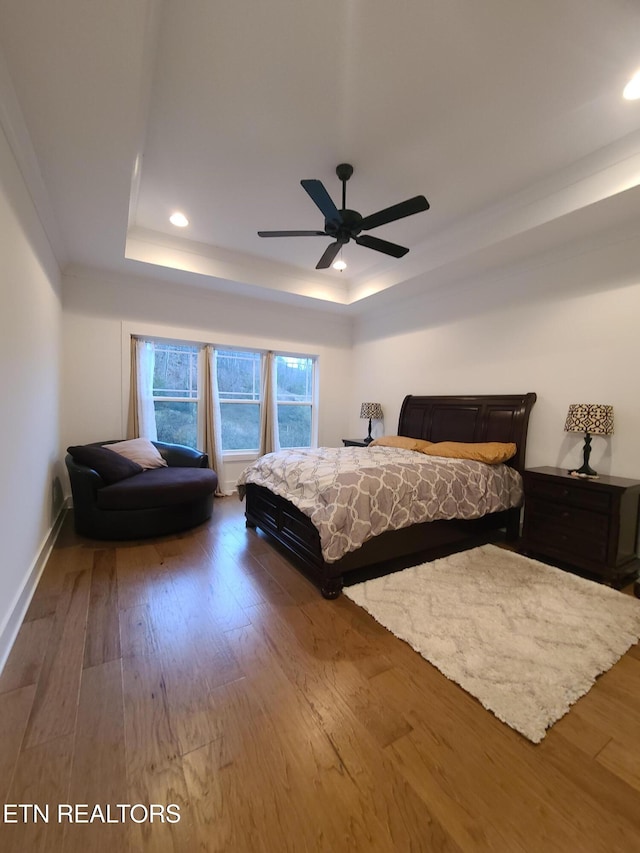 bedroom featuring a ceiling fan, a tray ceiling, wood finished floors, and baseboards