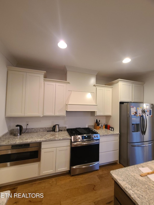 kitchen featuring wood finished floors, recessed lighting, custom range hood, white cabinets, and appliances with stainless steel finishes