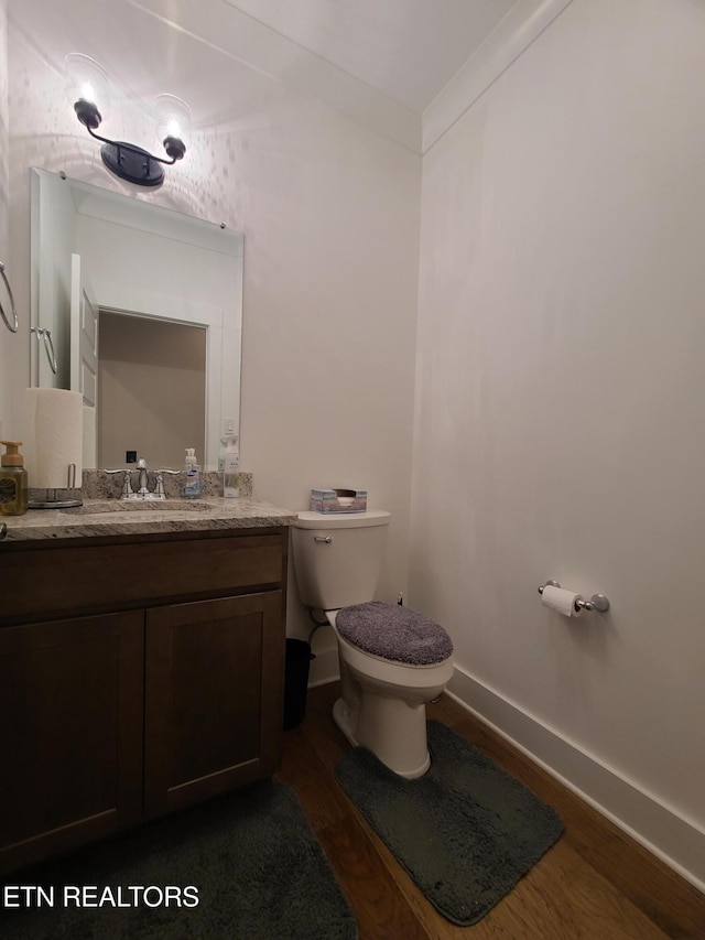 bathroom with toilet, ornamental molding, wood finished floors, baseboards, and vanity