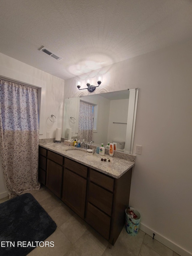 full bath featuring visible vents, a textured ceiling, vanity, and baseboards