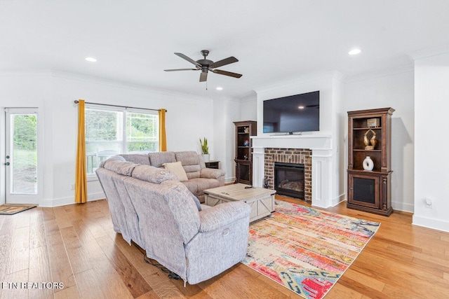 living room featuring crown molding, light wood-type flooring, a brick fireplace, and ceiling fan