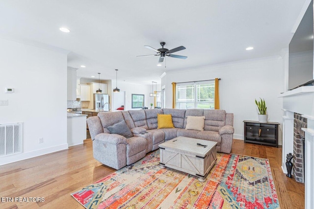 living area featuring light wood-style flooring, a ceiling fan, crown molding, visible vents, and recessed lighting
