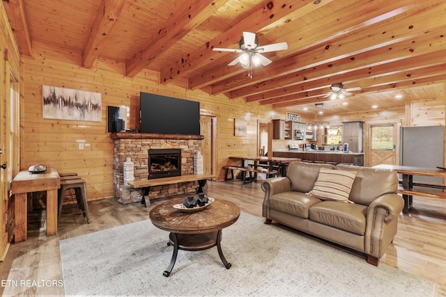 315 Caney Creek Rd, Pigeon Forge, TN 37863 - living room featuring ceiling fan, light wood-type flooring, beamed ceiling, a stone fireplace, and wood walls