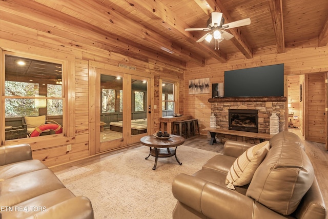 living room featuring a fireplace, wood walls, beam ceiling, and ceiling fan