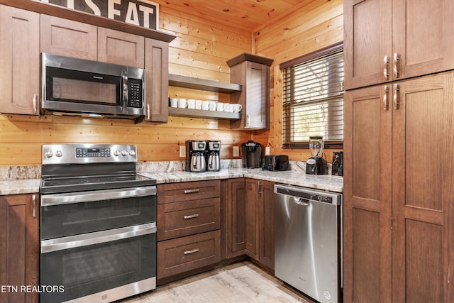 kitchen featuring light stone countertops, stainless steel appliances, wooden walls, and light hardwood / wood-style flooring