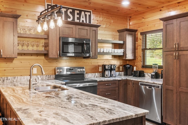 kitchen with wood walls, sink, stainless steel appliances, and light stone counters