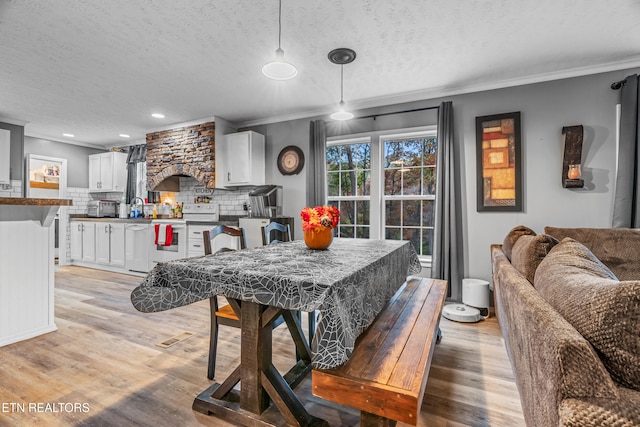 dining space featuring sink, ornamental molding, a textured ceiling, and light wood-type flooring