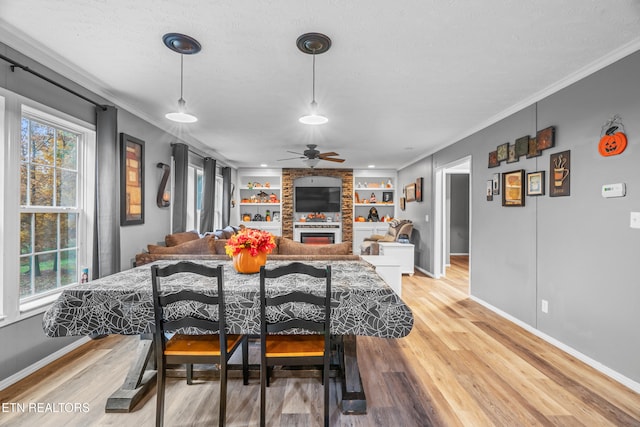 dining space with ceiling fan, light hardwood / wood-style floors, a stone fireplace, and crown molding