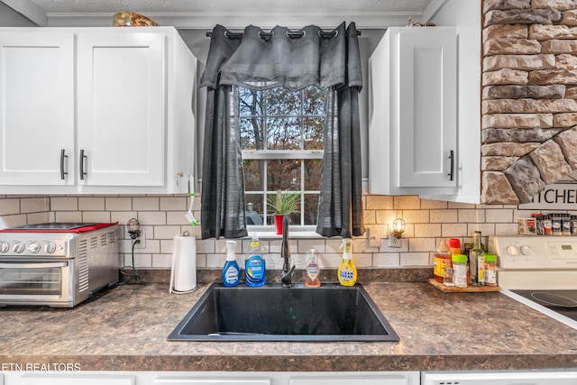 kitchen featuring backsplash, a textured ceiling, sink, white stove, and white cabinetry