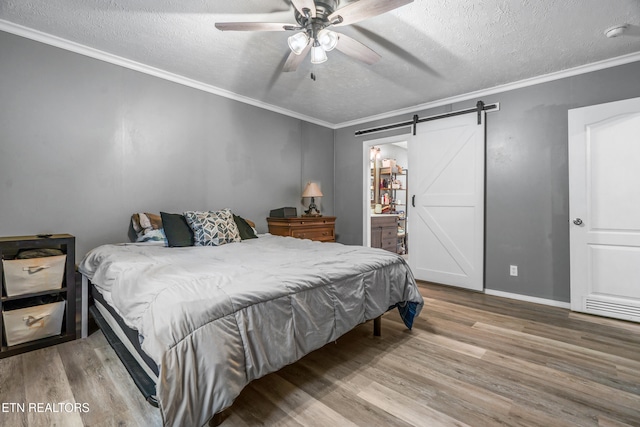 bedroom featuring ceiling fan, a barn door, hardwood / wood-style floors, a textured ceiling, and ornamental molding