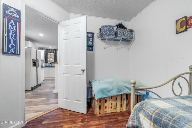 bedroom with dark hardwood / wood-style flooring, white refrigerator with ice dispenser, and a textured ceiling