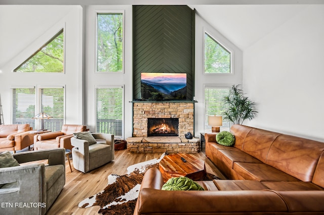 living room featuring a high ceiling, light wood-type flooring, and a stone fireplace