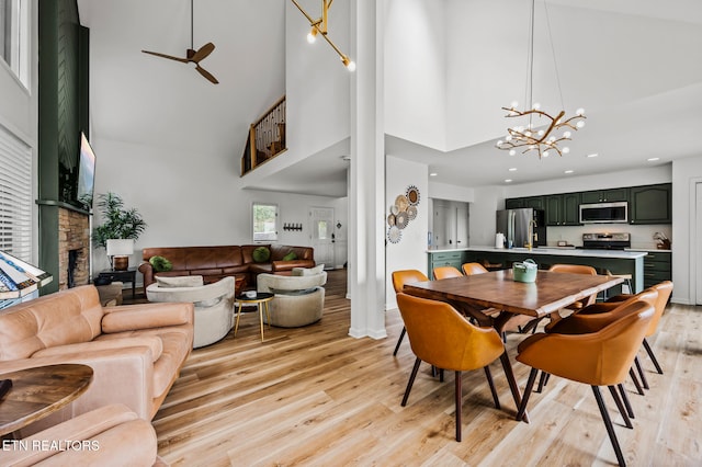 dining area with ceiling fan with notable chandelier, a towering ceiling, a fireplace, and light hardwood / wood-style flooring