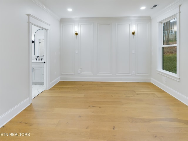 unfurnished room featuring visible vents, light wood-style floors, ornamental molding, a sink, and baseboards