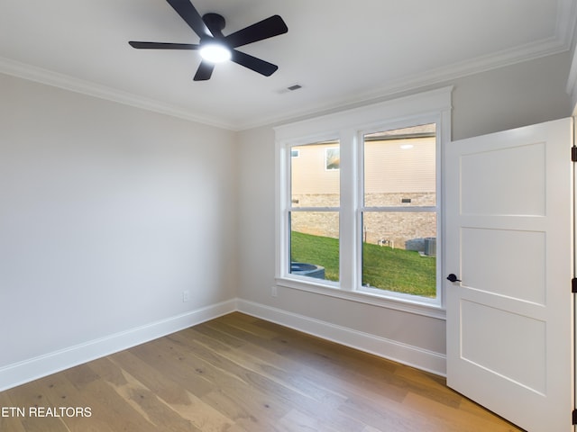 empty room with ornamental molding, wood finished floors, visible vents, and baseboards