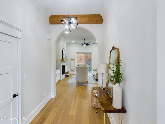 hallway featuring arched walkways, baseboards, light wood-style flooring, an inviting chandelier, and crown molding