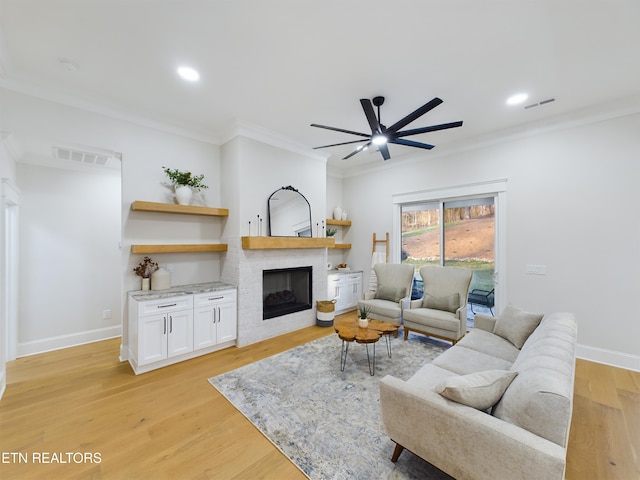 living area with visible vents, baseboards, light wood-style flooring, crown molding, and a brick fireplace