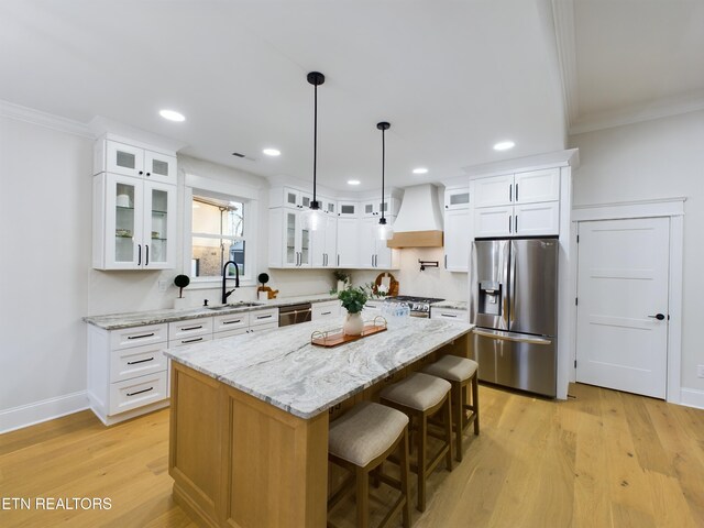 kitchen featuring custom range hood, appliances with stainless steel finishes, ornamental molding, light wood-type flooring, and a sink